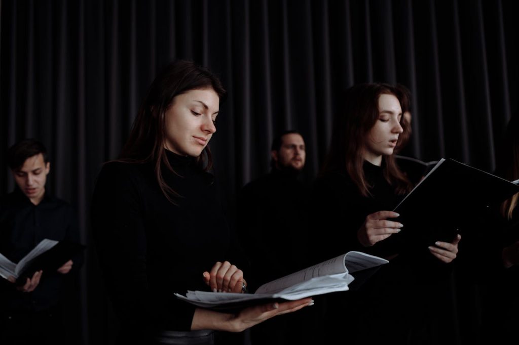 A group of people reading music sheets during an indoor choir practice session.