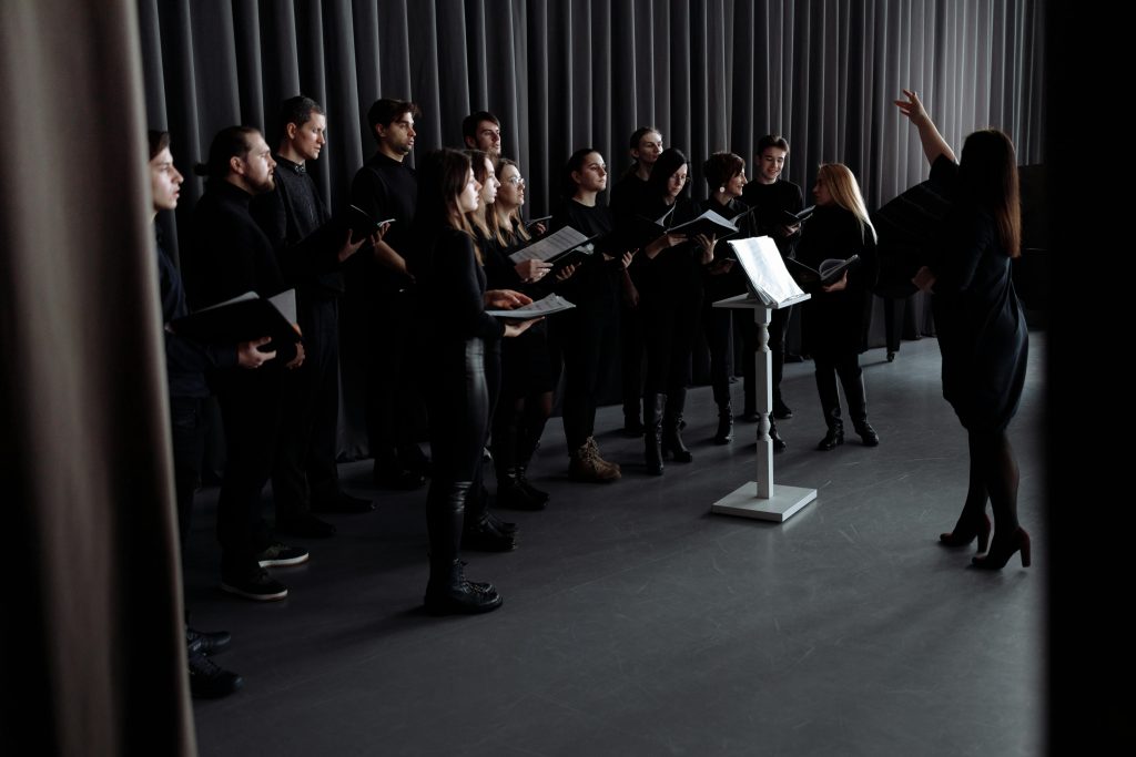 A choir practicing under a conductor's guidance in an indoor studio setting.