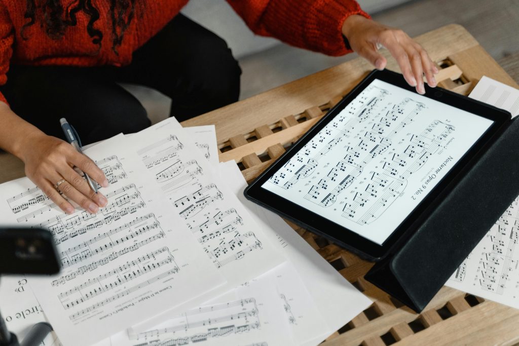 A person reviewing and composing sheet music using both paper and digital formats on a table.